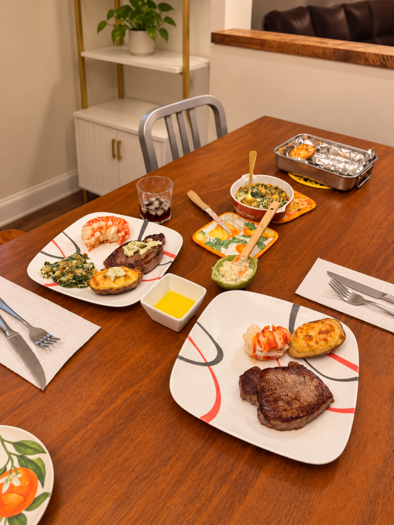 Steak and lobster dinner with twice-baked potatoes and spinach gratin set on a wooden family dining table.